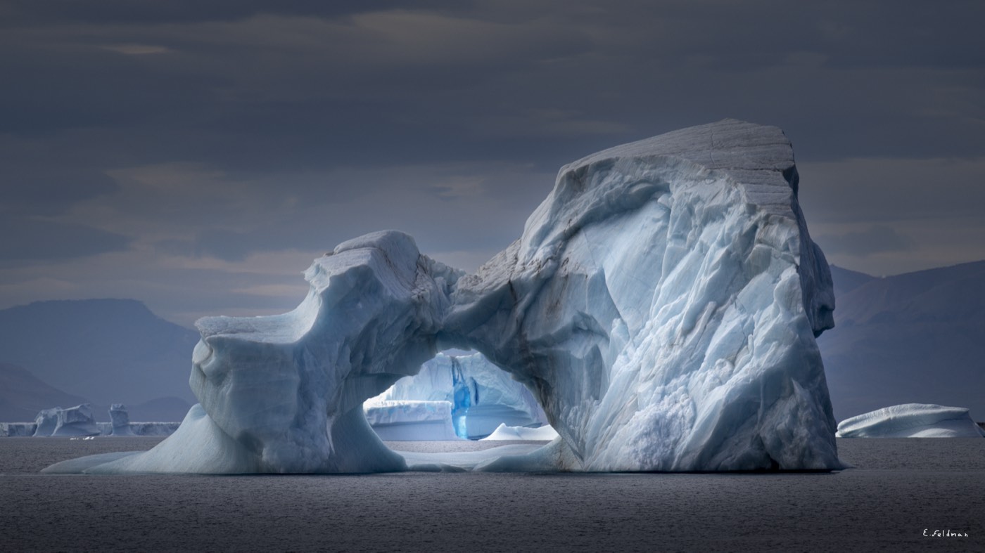 An iceberg with an arch and blue light inside