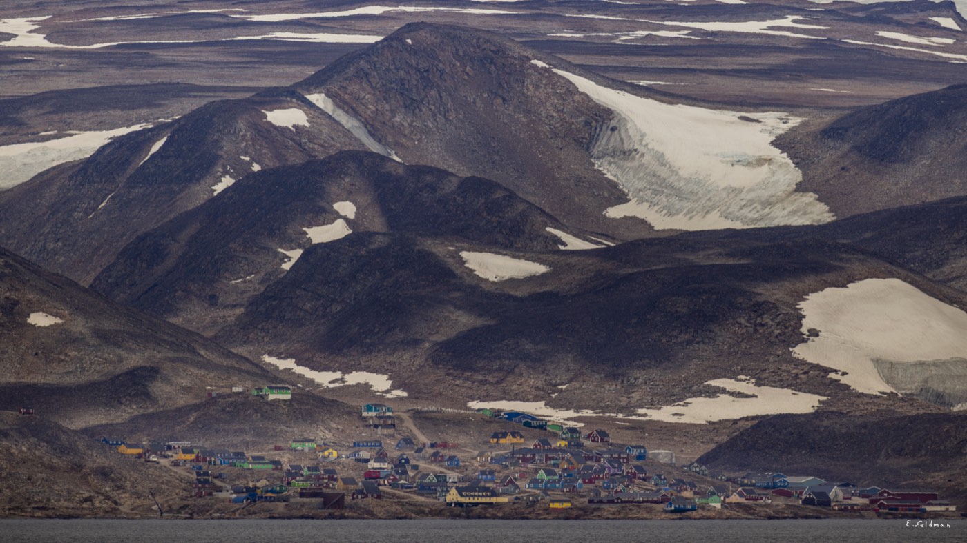 A village of colorful houses below snowy mountains, Greenland