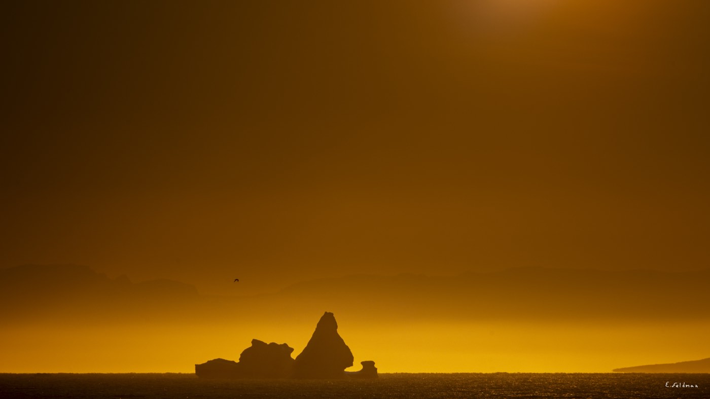 An iceberg silhouetted against an amber sky